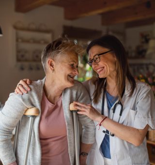 front-view-healthcare-worker-caregiver-visiting-senior-woman-indoors-home-helping-her-walk