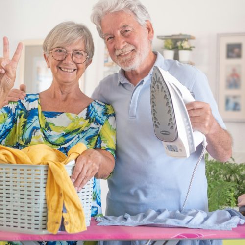 Senior man helps with household chores by ironing clothes on the ironing board