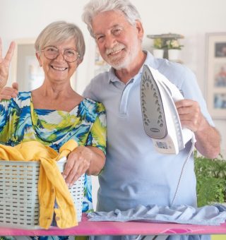 Senior man helps with household chores by ironing clothes on the ironing board